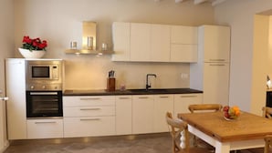 Una cocina moderna con armarios blancos, horno integrado, microondas y una mesa de comedor de madera con sillas.
