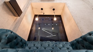 A modern interior with a tufted blue sofa and a geometric light fixture above a glass door. - PC Boutique H Loggia by ClaPa Group Dislocated Hospitality (Naples)
