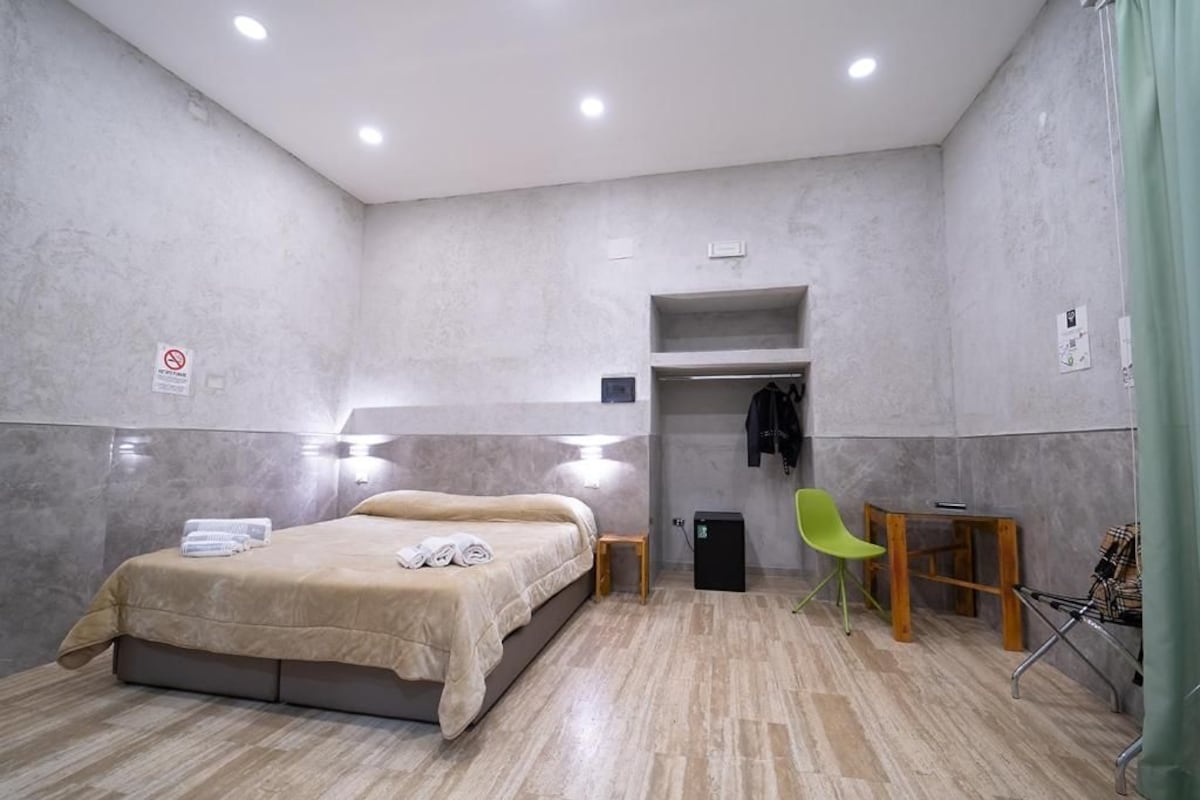 A hotel room with a bed, a small table, a chair, and a wardrobe.