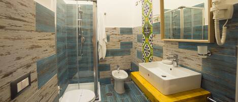 A bathroom with a glass-enclosed shower, a toilet, a bidet, and a sink with a mirror above it.