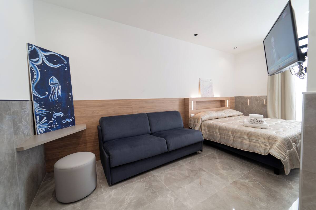 Ein modernes Hotelzimmer mit einer Couch, einem Bett, einem Flachbildfernseher und Kunstwerken an der Wand.