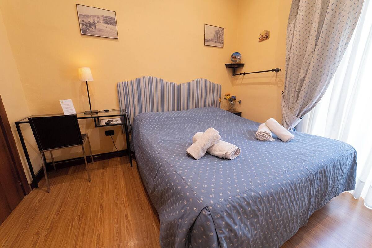 Ein Hotelzimmer mit einem Bett, einem Schreibtisch mit Stuhl, einer Lampe und einem Fenster mit Vorhängen.
