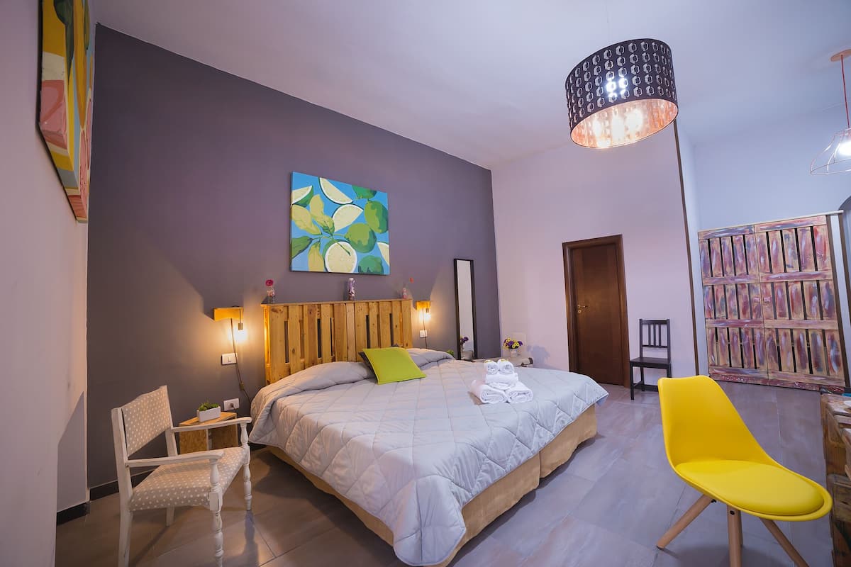 Ein Schlafzimmer mit einem Bett, einem Sessel, einem Nachttisch, einer Lampe und einem Bild an der Wand.