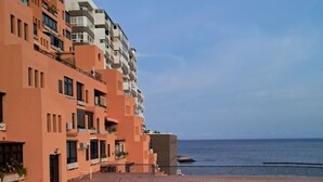 Una piscina contigua a un edificio de varios pisos con balcones, con vista a una masa de agua.