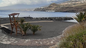 Una playa con costa rocosa, una estructura de madera y vista al mar y colinas distantes.