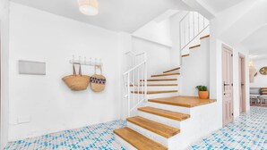 Una escalera con escalones de madera que conduce a una plataforma, una pared blanca con una cesta colgante y un suelo estampado.