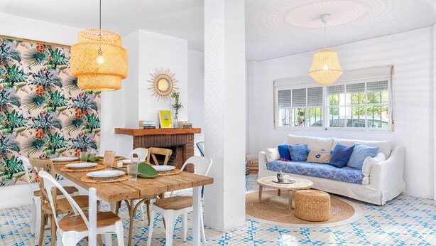 Un comedor con mesa y sillas de madera, un sofá blanco y piso estampado.
