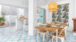 Comedor con mesa de madera dispuesta para cuatro, sillas blancas y un papel tapiz tropical.