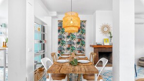 Comedor con mesa de madera, sillas blancas y papel tapiz tropical.