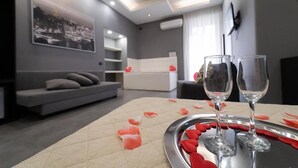 A modern living room with a sofa, a coffee table with rose petals and glasses, and a cityscape painting on the wall. - Royal House Napoli Centro "by ClaPa Group Dislocated Hospitality (Naples)