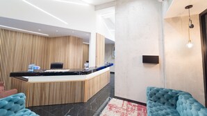 A modern reception area with a wooden reception desk, a black marble counter, and a blue upholstered chair. - Royal House Napoli Centro "by ClaPa Group Dislocated Hospitality (Naples)