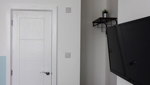 A room with a white door, a black cabinet, and a small shelf with a plant. - Apartments St Thomas Road (Chorley)