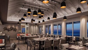 A spacious dining area with multiple tables and chairs, large windows offering a view of the ocean, and pendant lighting. - Luxury Condo with spectacular amenities on Paradise Island (Paradise Island, Nassau)