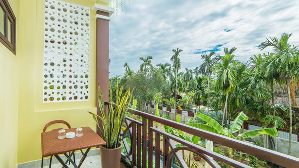 A balcony with a table and chairs, a potted plant, and a view of a lush garden with palm trees. - A Bong Villa (Da Nang)