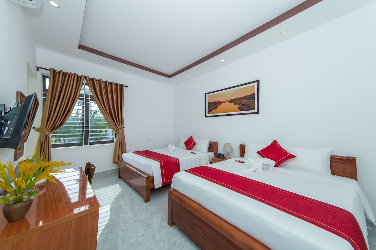 A hotel room with two beds, a desk, a TV, and a window with curtains.