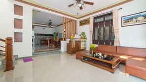 A spacious living room with a sofa, coffee table, and a ceiling fan. A kitchen is visible in the background. - A Bong Villa (Da Nang)