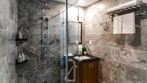 A modern bathroom with a glass-enclosed shower, marble walls, a wooden cabinet, and a towel rack. - A Bong Villa (Da Nang)