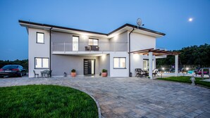 Ein modernes, zweistöckiges Haus mit Balkon, überdachter Terrasse und Auffahrt.