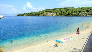 Une plage avec une eau cristalline, des gens qui se baignent et prennent des bains de soleil, et un bateau amarré sur la gauche.