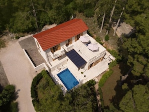 A two-story house with a red-tiled roof, a swimming pool, and a covered patio area.