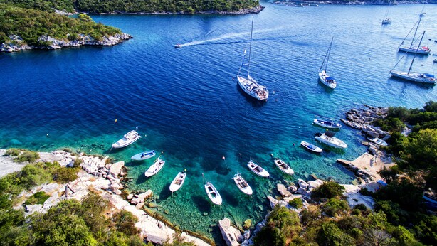 Un port de plaisance situé sur la côte, où des bateaux sont amarrés et ancrés, entouré d’un paysage rocheux et d’une végétation luxuriante.