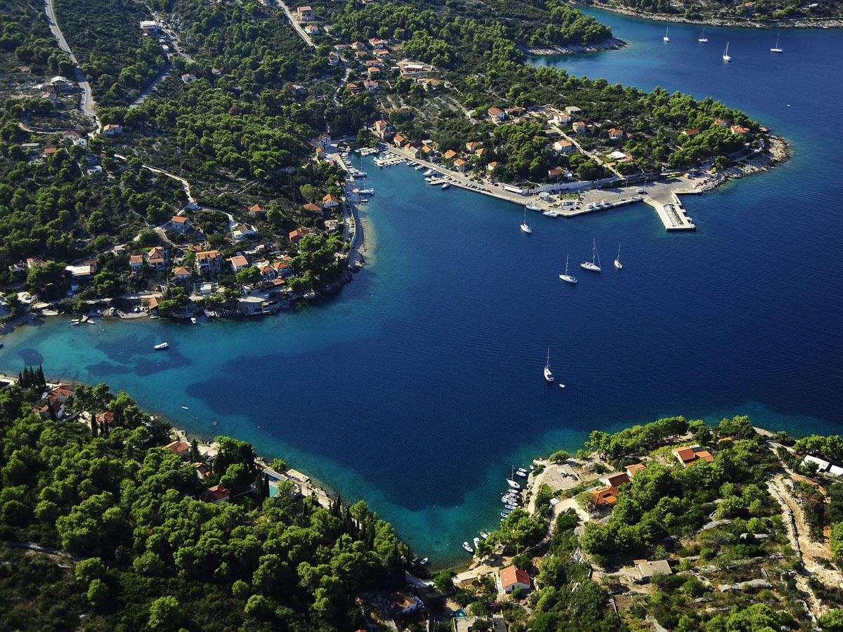 An aerial view of a coastal town with a marina, surrounded by lush greenery and clear blue waters.
