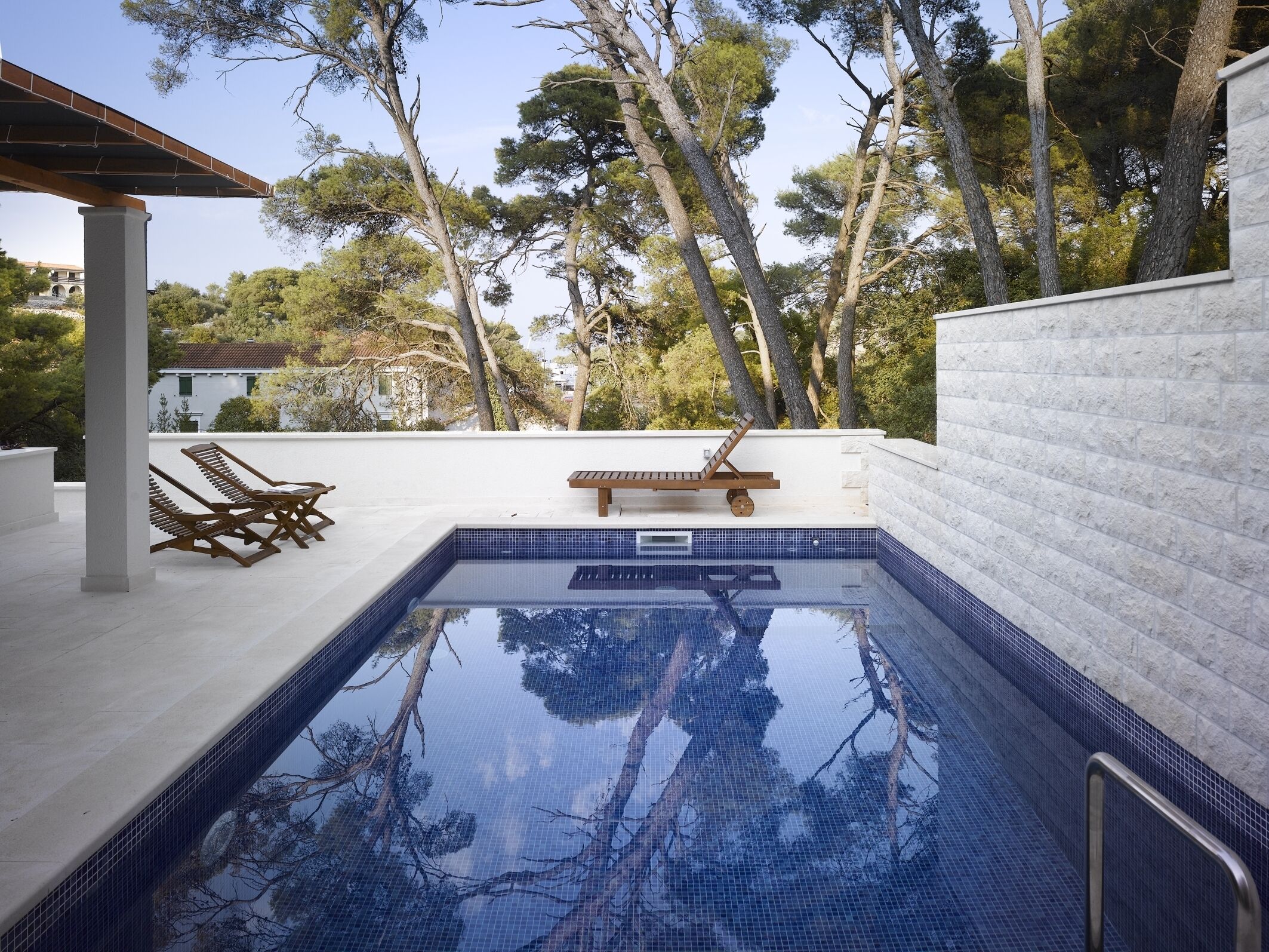 A swimming pool with a tiled deck, lounge chairs, and a wooden bench.