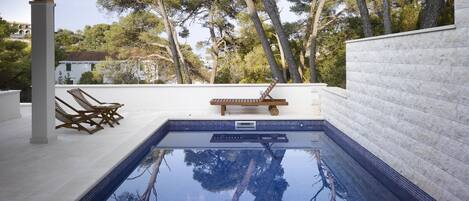 A swimming pool with a tiled deck, lounge chairs, and a wooden bench.