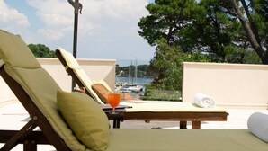 A sun lounger with a cushion, a glass of orange juice, and a rolled towel on a balcony overlooking a marina. - LUXURY: VILLA on the SEA, POOL & BEACH BIKE & KAYAK & PRESENT (Rogac)