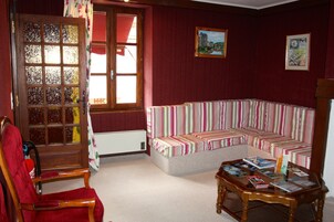 Un salón acogedor con un sillón rojo, un sofá a rayas y una mesa de centro de madera con revistas.
