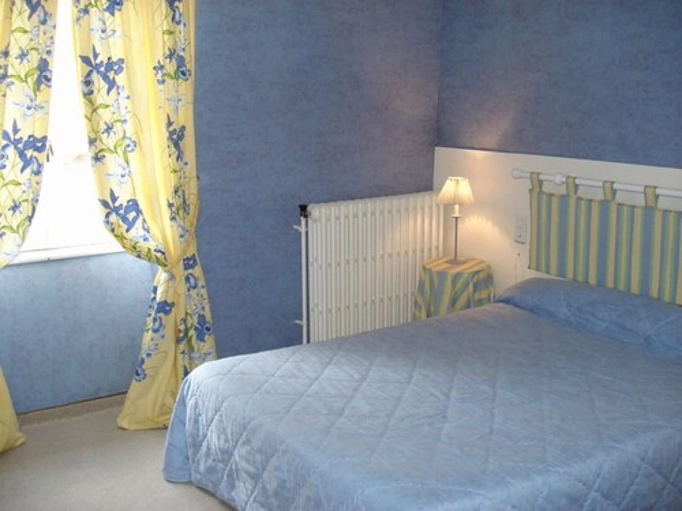 A bedroom with a bed, a radiator, a lamp on a bedside table, and curtains.