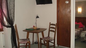 A small room with a table, two chairs, a TV mounted on the wall, and a door leading to another room. - Auberge Aux Portes de Conques (Conques-en-Rouergue)