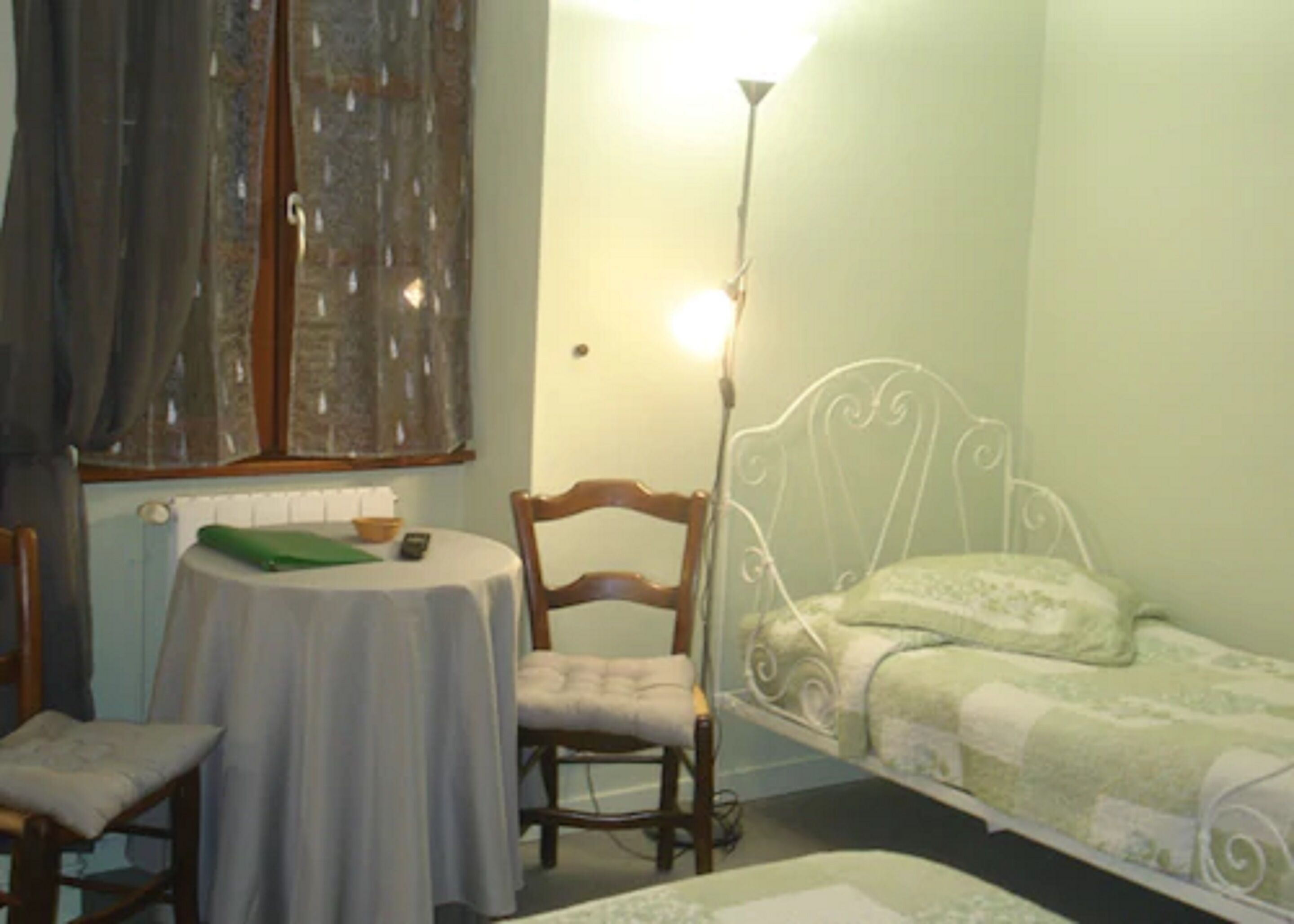 A small room with a single bed, a chair, a table, and a lamp.