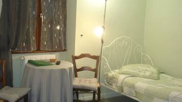A small room with a single bed, a chair, a table, and a lamp.
