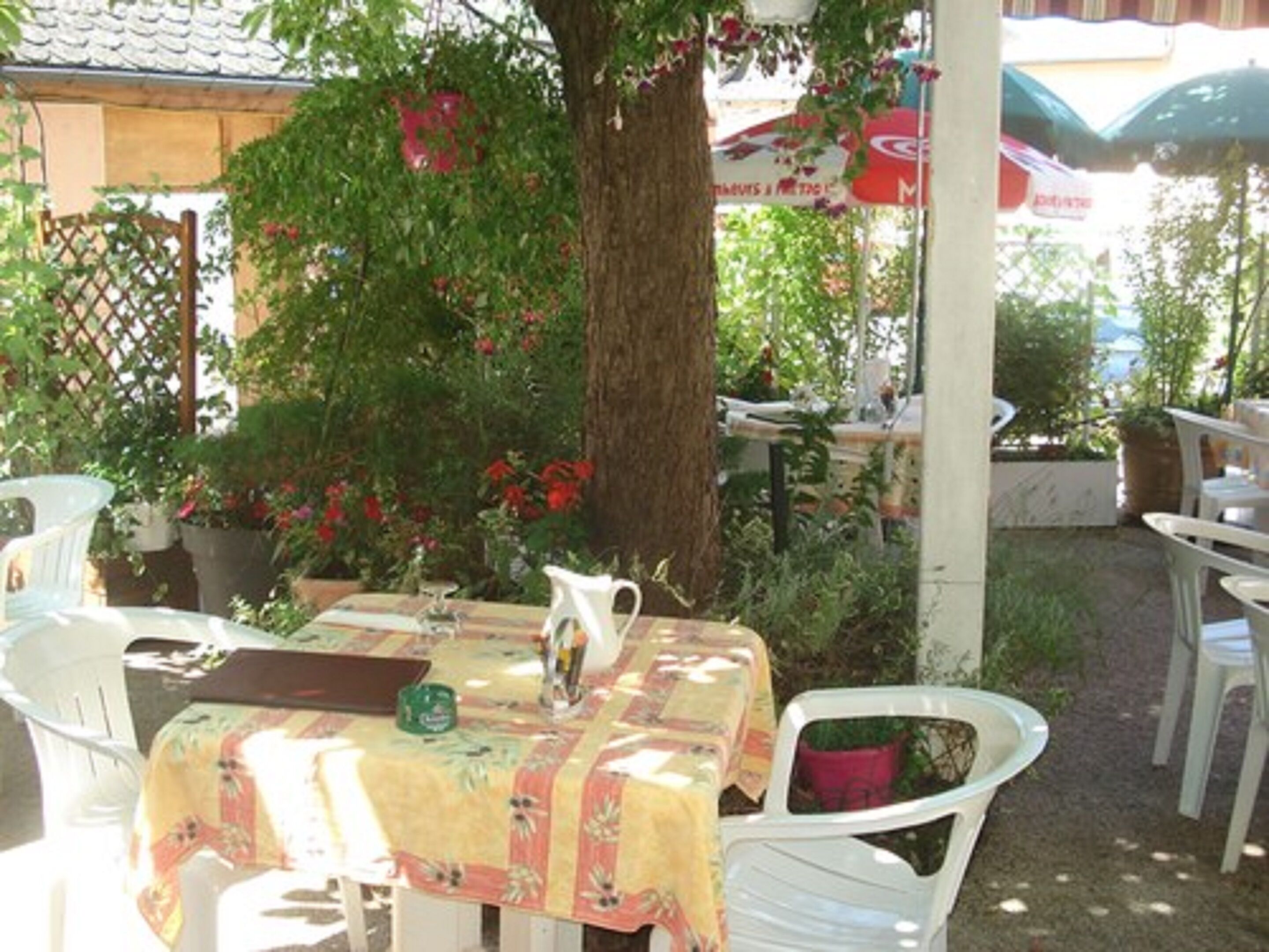 An outdoor patio with white plastic chairs and a table covered with a floral tablecloth.