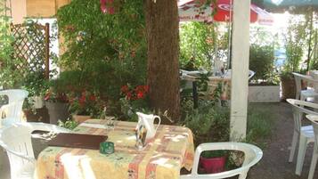 An outdoor patio with white plastic chairs and a table covered with a floral tablecloth.