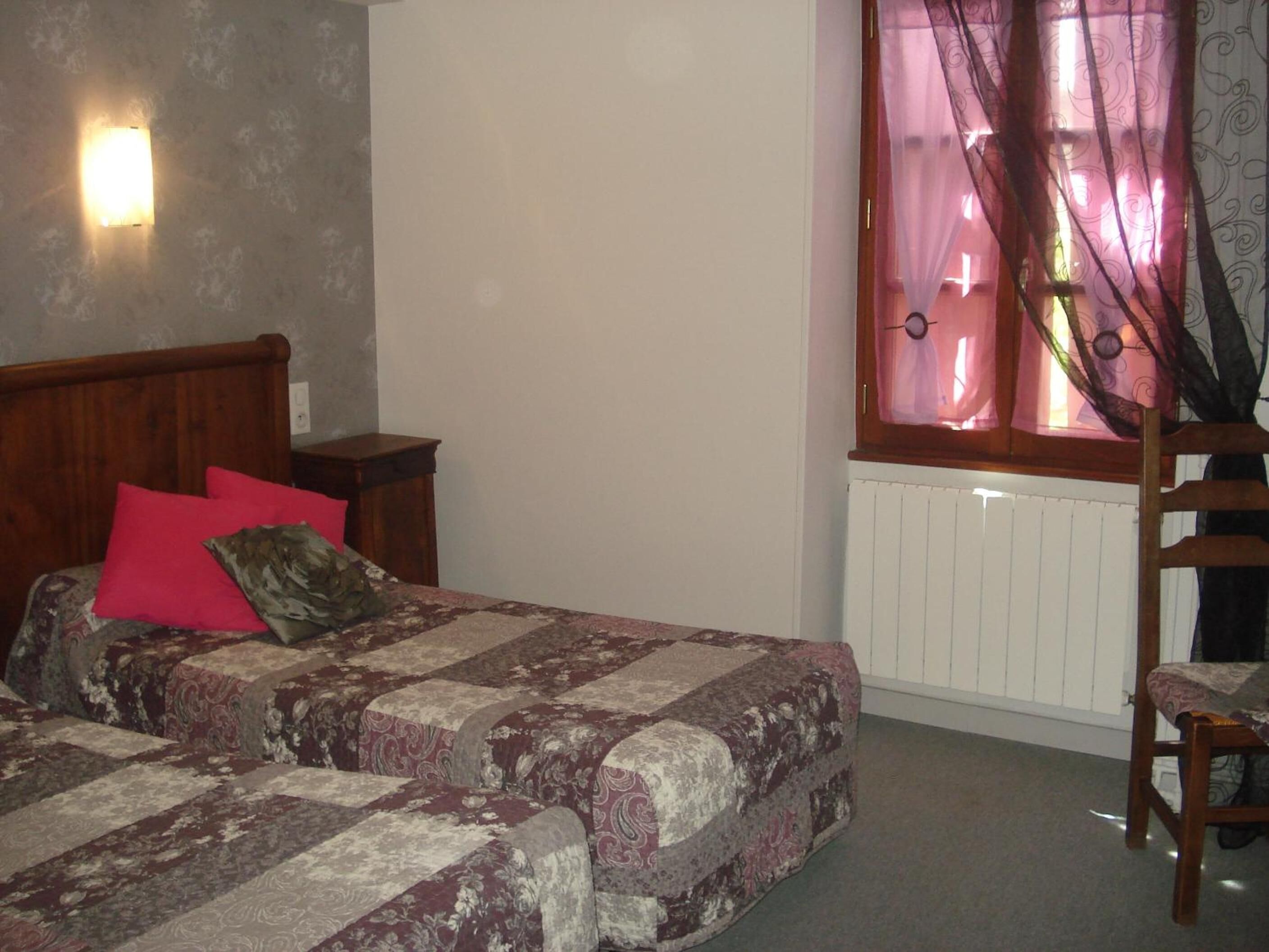 Un dormitorio con cama, mesita de noche, silla y ventana con cortinas.