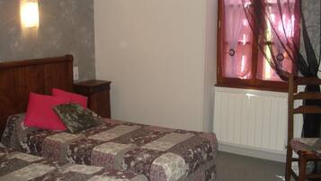 Un dormitorio con cama, mesita de noche, silla y ventana con cortinas.