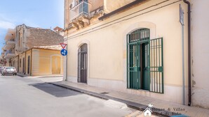 A street with a building featuring a green gate, a blue sign with a white arrow, and a no parking sign.