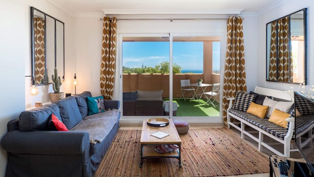 A living room with a sofa, a coffee table, and a patterned rug. There is a sliding glass door leading to an outdoor area with a view of the sea. - SUPERB APARTMENT WITH SEA VIEW AND ELVIRIA GOLF COURSE (Marbella)