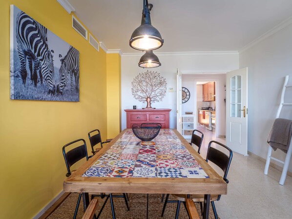 A dining area with a long wooden table, chairs, a patterned tablecloth, and a zebra painting on the wall.