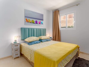 A bedroom with a bed, bedside tables, a nightstand, a window with curtains, and a wall art piece.
