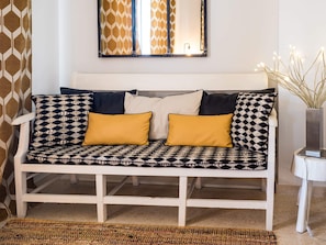 A white sofa with patterned cushions, a woven rug, and a mirror above it.