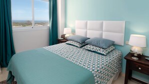 A bedroom with a bed, two bedside tables, a window with curtains, and a view of the city. - SUPERB APARTMENT WITH SEA VIEW AND ELVIRIA GOLF COURSE (Marbella)