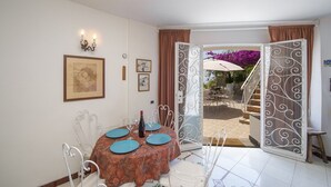 A dining area with a round table set for four, a staircase leading to an outdoor patio, and a view of the outdoors. - Casa Albatros (Praiano)