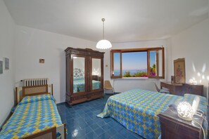 A bedroom with two beds, a wardrobe, a window with a view, and a ceiling light.