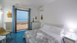 A hotel room with a bed, a nightstand, a dresser, a chair, and a view of the beach through an open door. - Casa Albatros (Praiano)