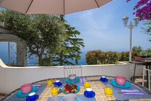 A table set for breakfast with a view of the sea, a pergola, and a street lamp.