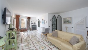 A living room with a sofa, a TV, a dining area with a table and chairs, and a kitchen area with a stove and cabinets. - Casa Albatros (Praiano)