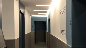 A modern hallway with a herringbone-patterned floor, recessed lighting, and a digital elevator display. - Ottaviano Smart Rooms (Rome)